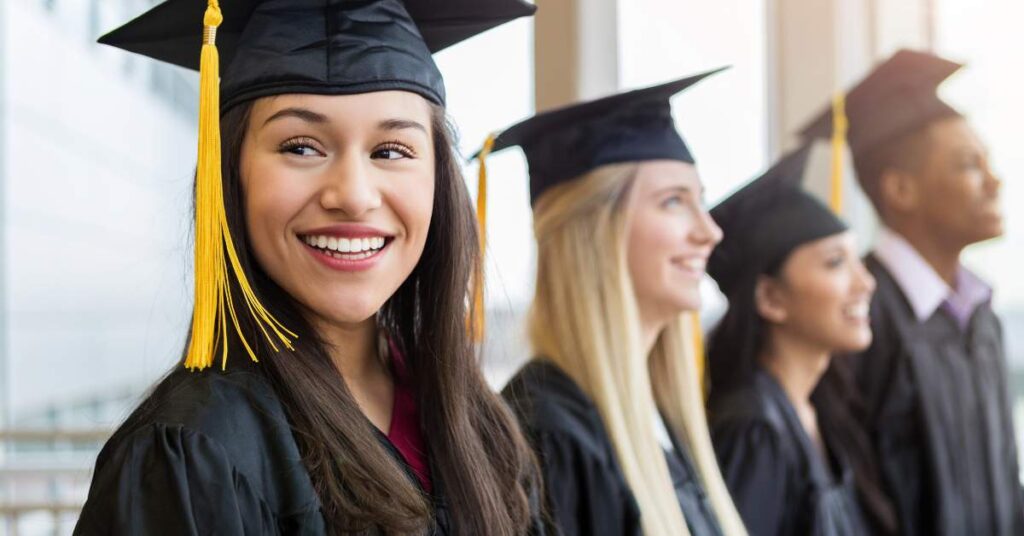 A line of three women and one man standing together wearing graduation caps and gowns.