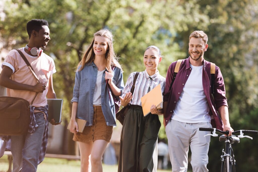 Diverse group of smiling college students walking together on a sunny campus path, carrying backpacks and books. This image illustrates the value of perseverance, specifically encouraging sophomores to re-file the FAFSA for potential financial aid opportunities they may have missed as freshmen. Source: The College Investor